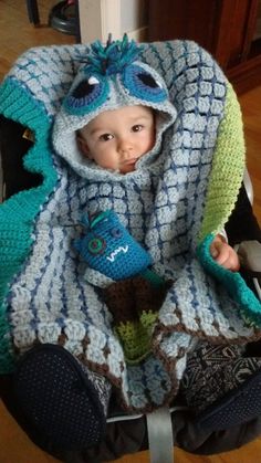 a baby sitting in a car seat wearing a crocheted blanket