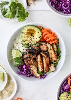 two white bowls filled with chicken, rice and veggies next to sliced avocado