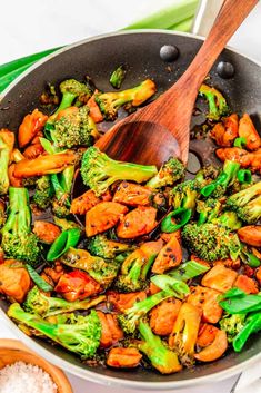 broccoli and chicken stir fry in a skillet with wooden spatulas