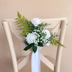 a bouquet of white roses and greenery sits on a chair in front of a wall