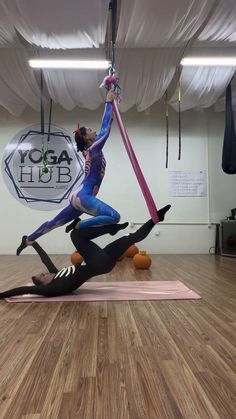 two women doing aerial acrobatics in an indoor gym with yoga mats on the floor