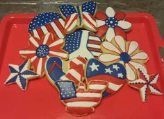 decorated cookies in the shape of american flags and flowers on a red tray with plastic wrappers