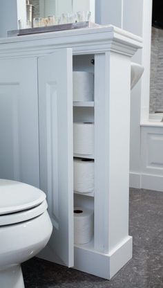 a white toilet sitting next to a cabinet with rolls of toilet paper on top of it