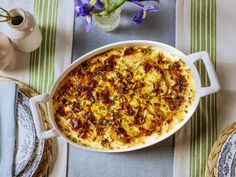 a casserole dish is sitting on a table with plates and flowers in the background