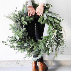 a woman is holding a wreath with greenery on it and her hands are in the center