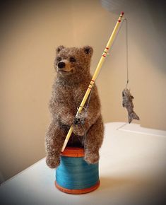 a brown teddy bear sitting on top of a blue cup holding a fishing rod and a fish