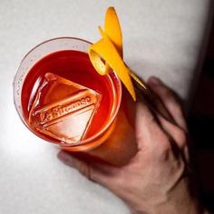 a hand holding a glass with some type of drink in it and an orange peel sticking out of the top