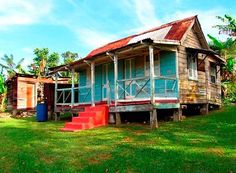 an old wooden house sitting in the middle of a lush green field with red steps leading up to it