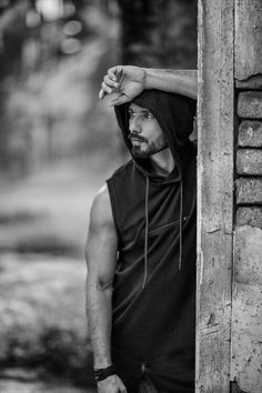 black and white photograph of a man leaning up against a wooden building with his hands on his head