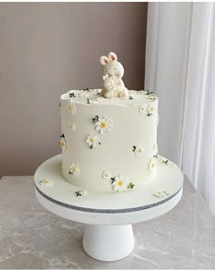 a white cake decorated with daisies and a bunny on top