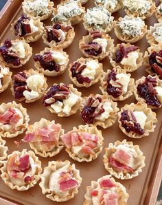 many small pastries are arranged on a baking sheet with cranberry sauce and pecans