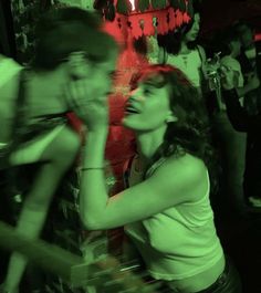 a group of people standing around in a room with red lights on the wall and one woman holding her hand up to her mouth