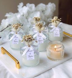 four small glass jars filled with candles on top of a white tray next to flowers