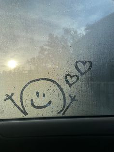 a smiley face drawn on the side of a car window with two hearts and crossbones