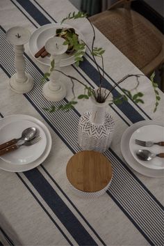 the table is set with plates, silverware and a vase filled with greenery