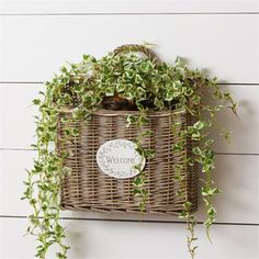 a wicker basket hanging on the wall with some plants in it and a welcome sign