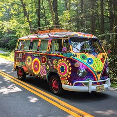 an old vw bus painted with bright colors driving down the road in front of trees