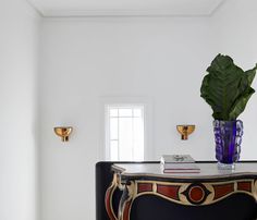 a vase with a plant on top of it next to a black and gold cabinet