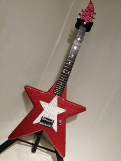 a red and white guitar with a pink star on it's neck, sitting on top of a stand