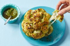 someone is dipping broccoli into some kind of sauce on a blue platter