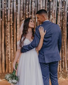 a bride and groom standing next to each other in front of a bamboo wall with lights