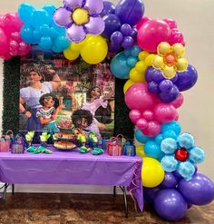 a birthday party with balloons and pictures on the wall, table set up in front of it