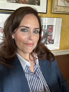 a woman wearing a blue blazer and white shirt posing for a photo in front of pictures on the wall