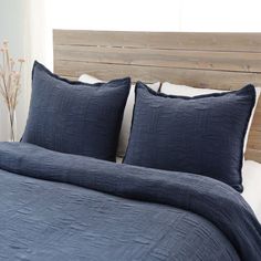 a bed with blue linens and pillows on it's headboard, in front of a window