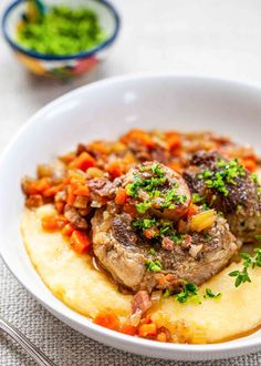 a white bowl filled with meat and veggies on top of mashed potatoes