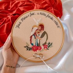 a woman is holding a cross - stitch hoop with the image of jesus and mary on it