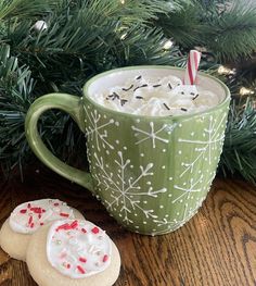 two cookies are next to a green mug with white frosting and candy canes