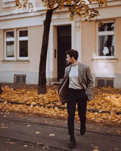 a man is walking down the street in front of a tree with leaves on it