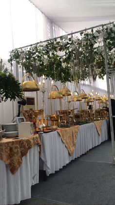 a buffet table is set up with gold and white plates, silver wares, and greenery