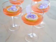 four glasses filled with different types of drinks and garnished with purple flowers on the rims