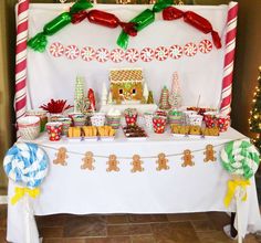 a table topped with lots of candy and candies next to a white wall covered in christmas decorations