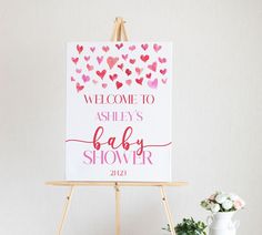 a baby shower sign sitting on top of a easel next to a potted plant