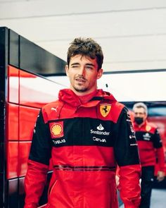 a man in a red and black racing suit standing next to a wall with ferrari logo on it