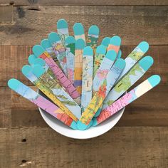 a white bowl filled with lots of colorful spoons on top of a wooden table