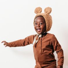 a little boy wearing a brown outfit and a mickey mouse hat with his arms out