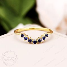 a gold ring with three blue sapphire stones on the front and side, sitting on top of a white box