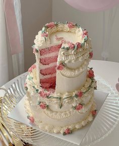 a three tiered cake with pink frosting and roses on it sitting on a plate