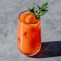 an orange cocktail garnished with parsley sits on a gray surface, ready to be served