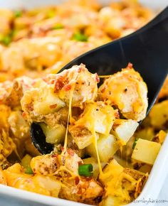 a spatula scooping food out of a casserole dish with potatoes and green onions