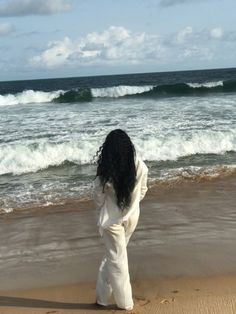 a woman standing on top of a sandy beach next to the ocean with waves coming in