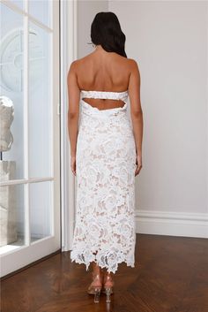 a woman in a white lace dress looking out the window with her back to the camera