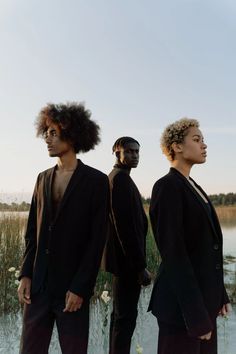 three men standing next to each other in front of a body of water and grass