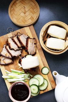 sliced meat and cucumbers on a wooden cutting board with sauce in a bowl