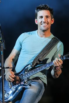 a man with a guitar and microphone in front of him smiling at the camera as he sings