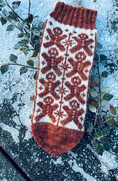 an orange and white knitted mitt sitting on top of snow covered ground next to plants