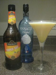 two bottles of alcohol and a martini glass on a counter top next to each other